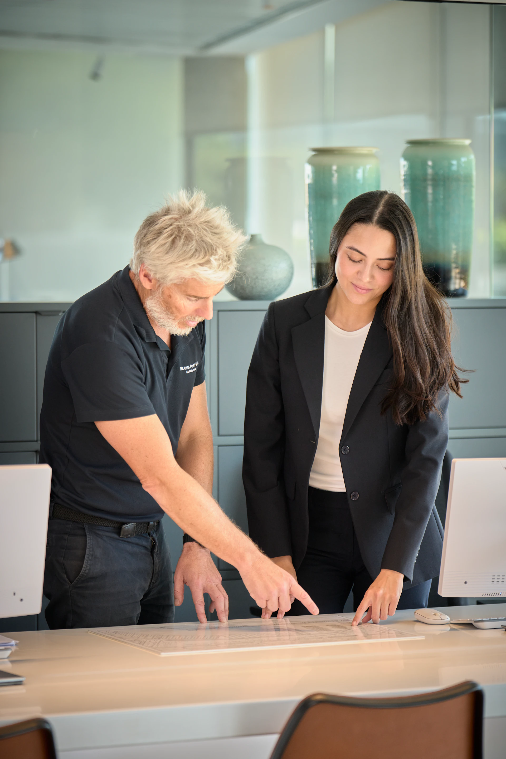 A man and woman in an office looking at a document on a desk.
