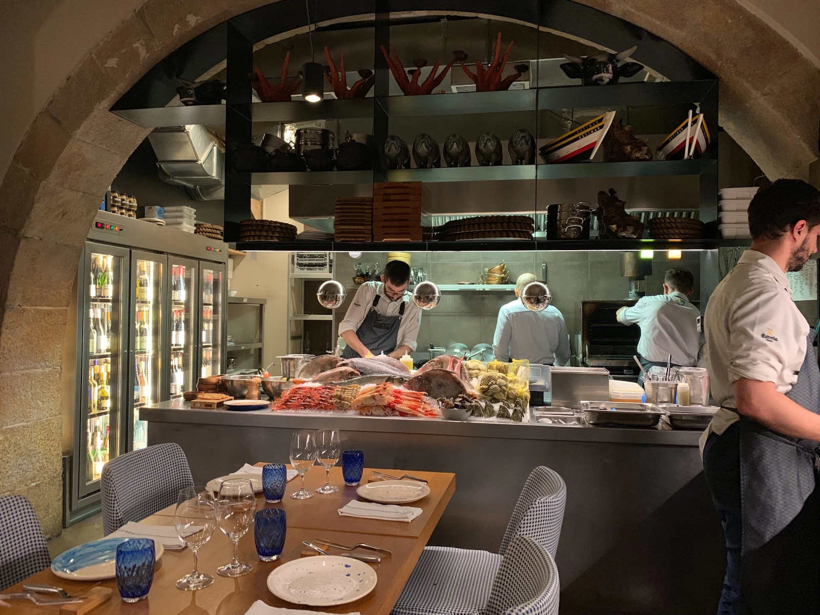 Chefs work in an open kitchen with fresh seafood display behind a set dining table.