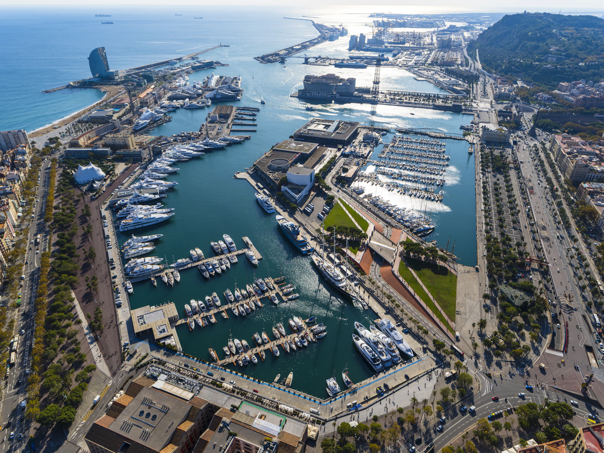 Vista aérea de Marina Port Vell que muestra superyates amarrados, embarcaciones atracadas y el paisaje urbano del frente marítimo de Barcelona.