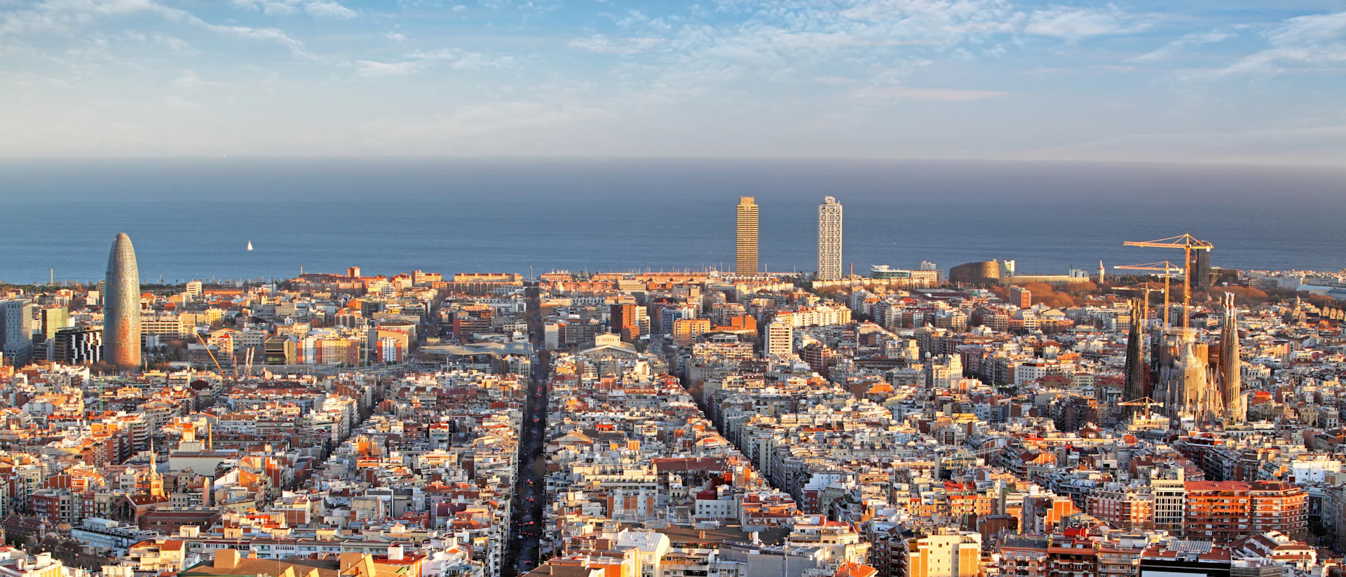 Vista aérea del paisaje urbano de Barcelona con edificios característicos, un denso desarrollo urbano y el horizonte del mar Mediterráneo.