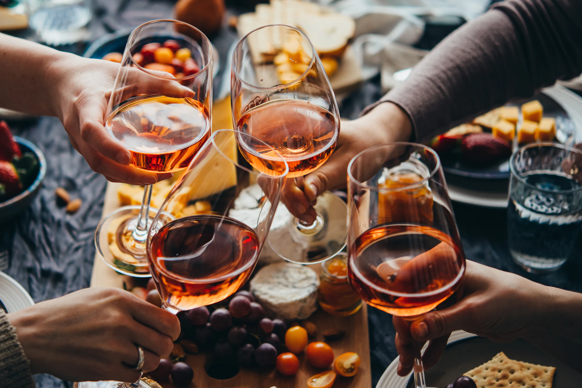 Varias personas brindando con copas de vino rosado sobre una mesa de comida y aperitivos.