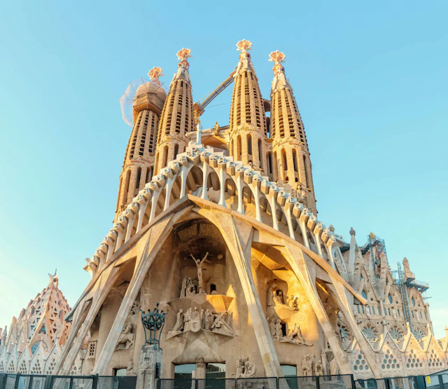 Sagrada Familia basilica with ornate golden spires and sculptural details against clear blue sky.