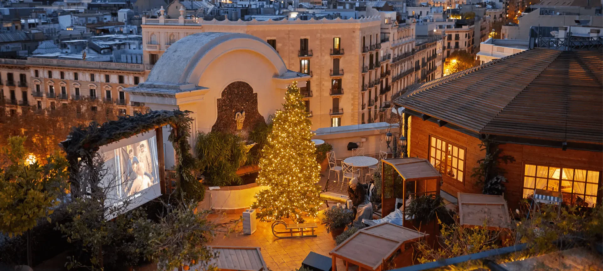 Terraza en la azotea con árbol de Navidad iluminado con vistas al Barrio Gótico de Barcelona al anochecer.