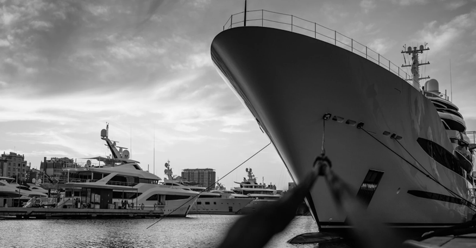 Large superyachts moored at a marina with city buildings visible in the background.