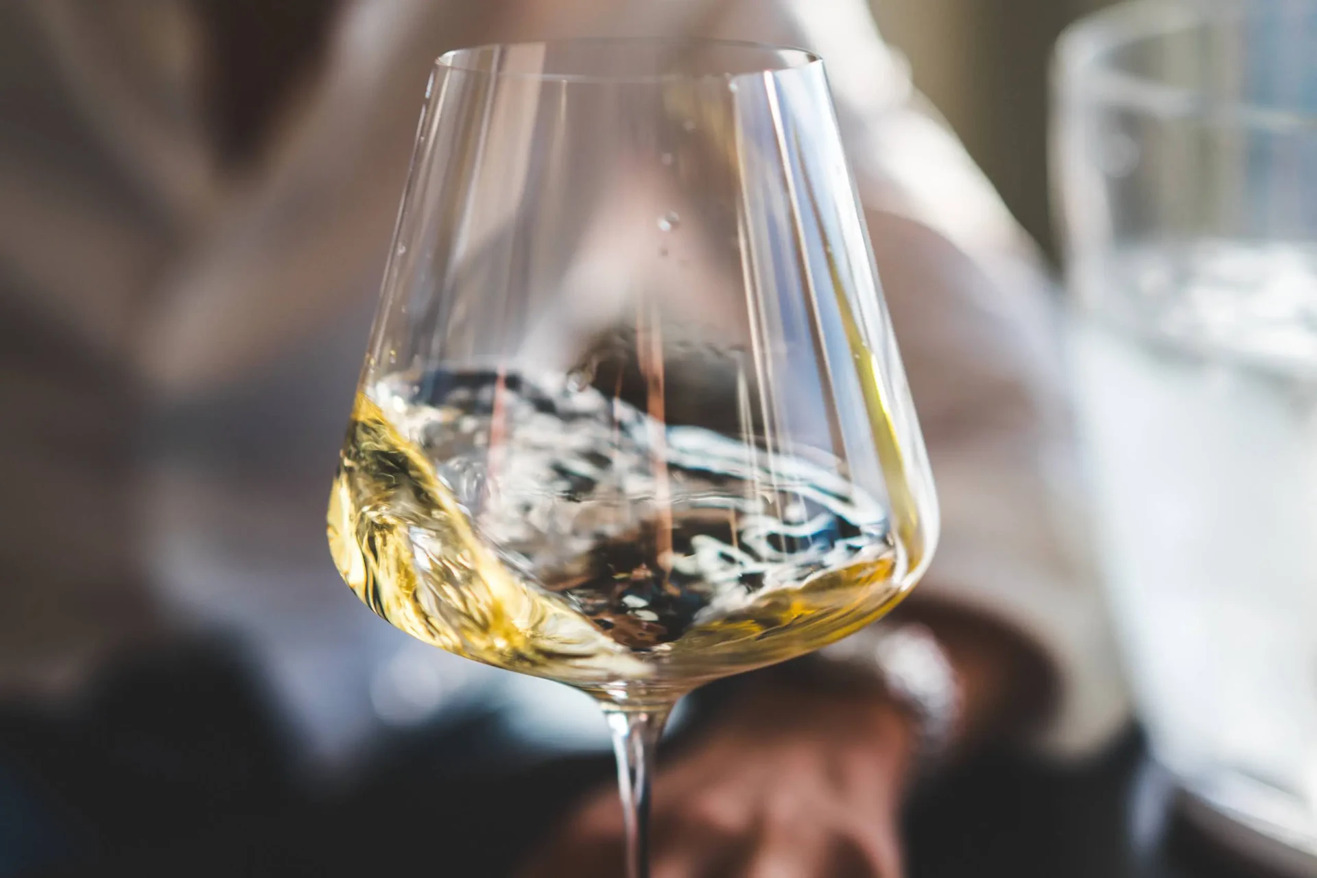 Copa de vino blanco sostenida al aire libre con un yate visible al fondo.