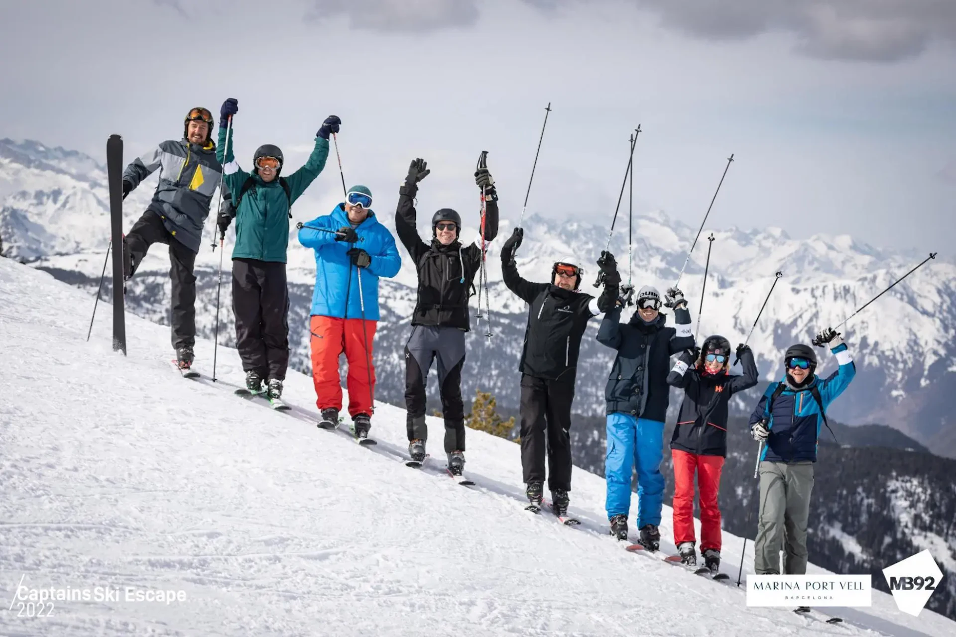 Grupo de esquiadores celebrando en una ladera nevada con picos cubiertos de nieve al fondo.