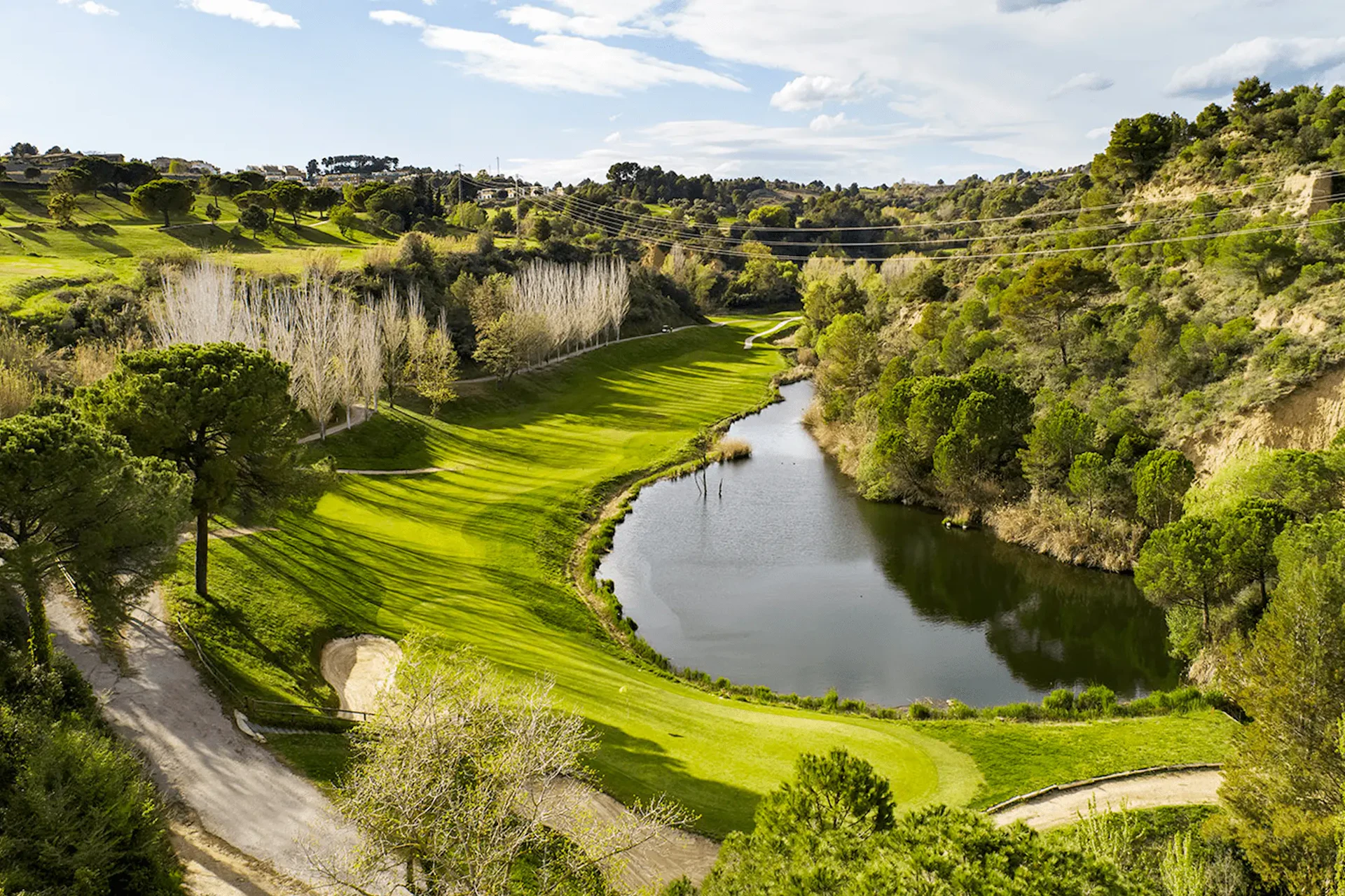 Valle verde y frondoso con un río serpenteante y laderas boscosas bajo un cielo azul.