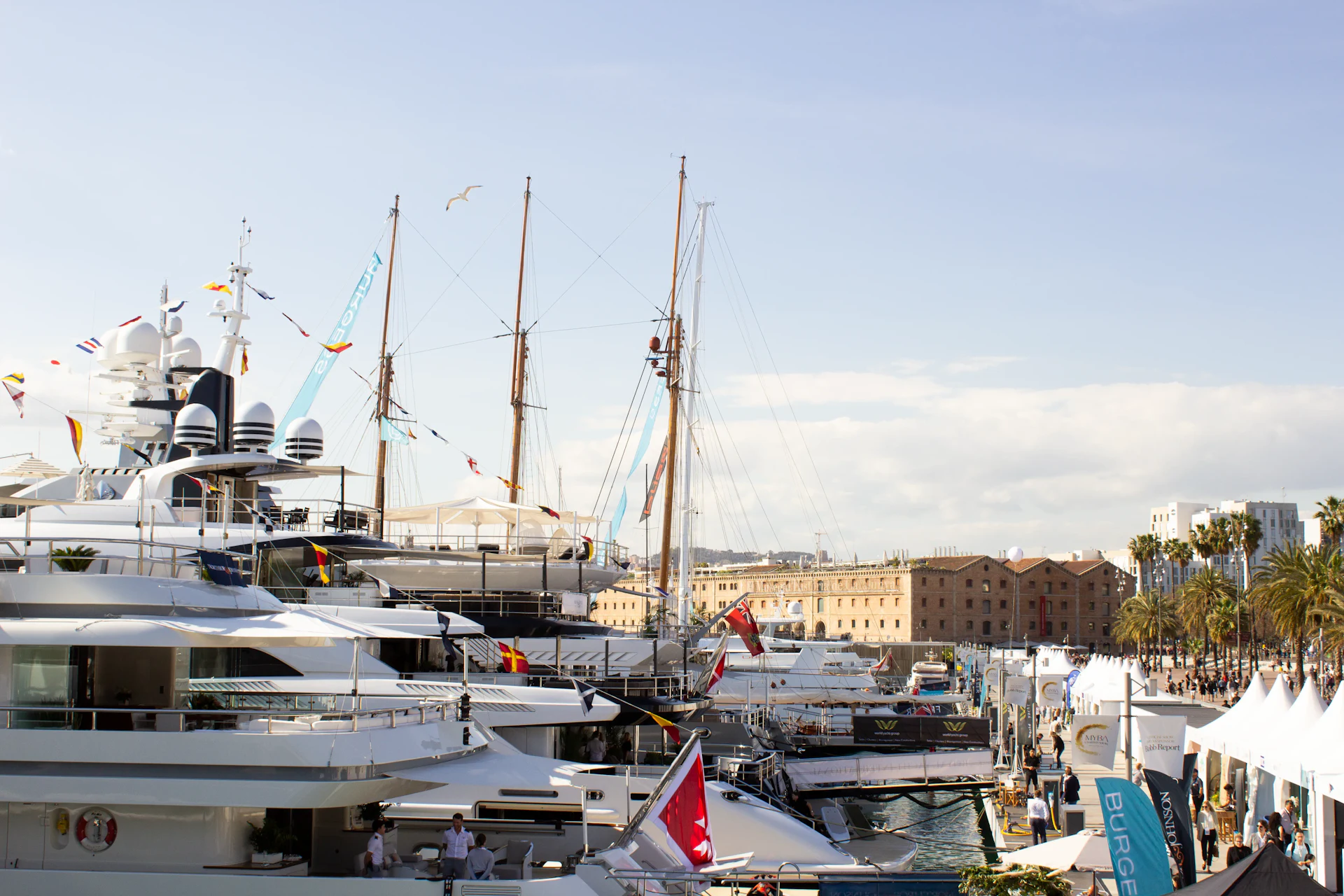 Superyates y grandes veleros amarrados en Marina Port Vell con los edificios del frente marítimo de Barcelona al fondo.
