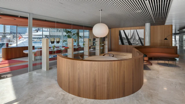 Modern reception area with curved wooden desk, pendant lighting, and marina views through floor-to-ceiling windows.