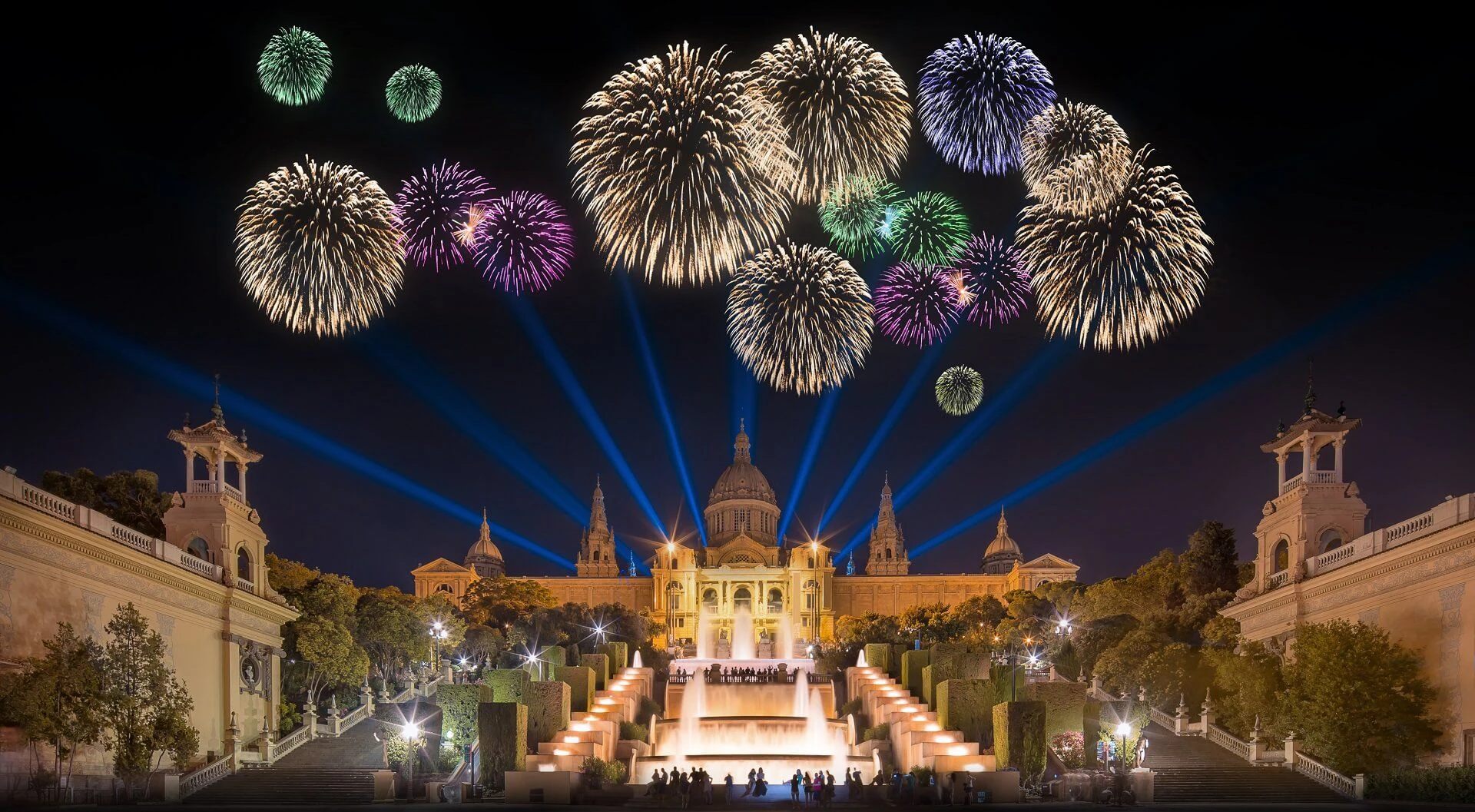 Coloridos fuegos artificiales estallan sobre una catedral y una plaza iluminadas de noche en Barcelona.
