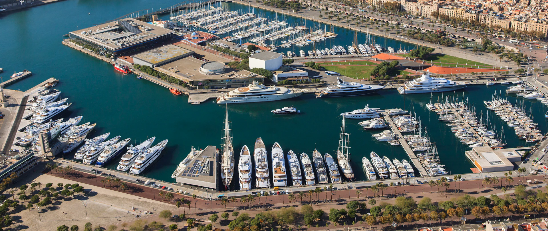 Vista aérea de Marina Port Vell que muestra varios yates blancos atracados en el puerto marítimo de Barcelona.