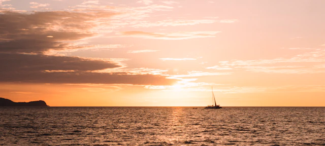 Velero en aguas tranquilas al atardecer con un espectacular cielo naranja y dorado.