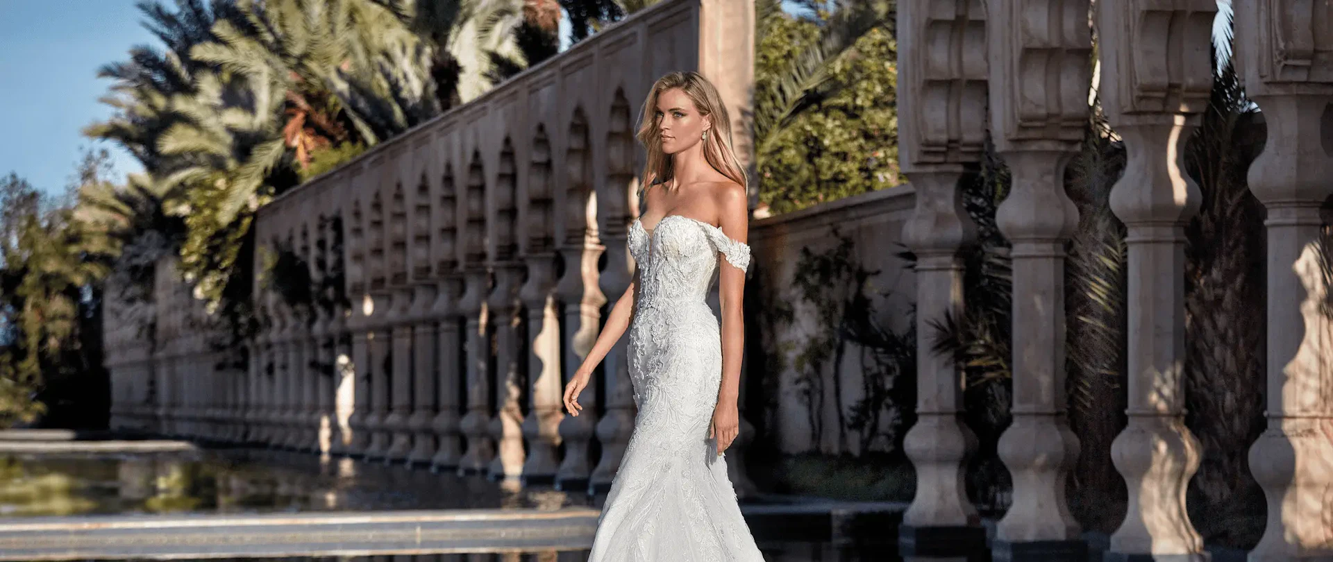 Mujer con vestido de novia blanco de hombros descubiertos de pie frente a una arquitectura clásica ornamentada.
