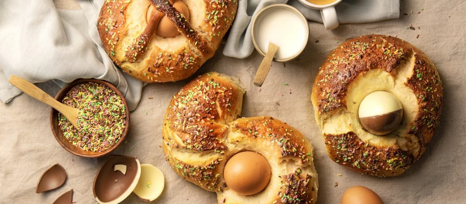 Bollos en forma de anillo recién horneados con huevos de chocolate y cobertura de pistacho sobre una superficie neutra.
