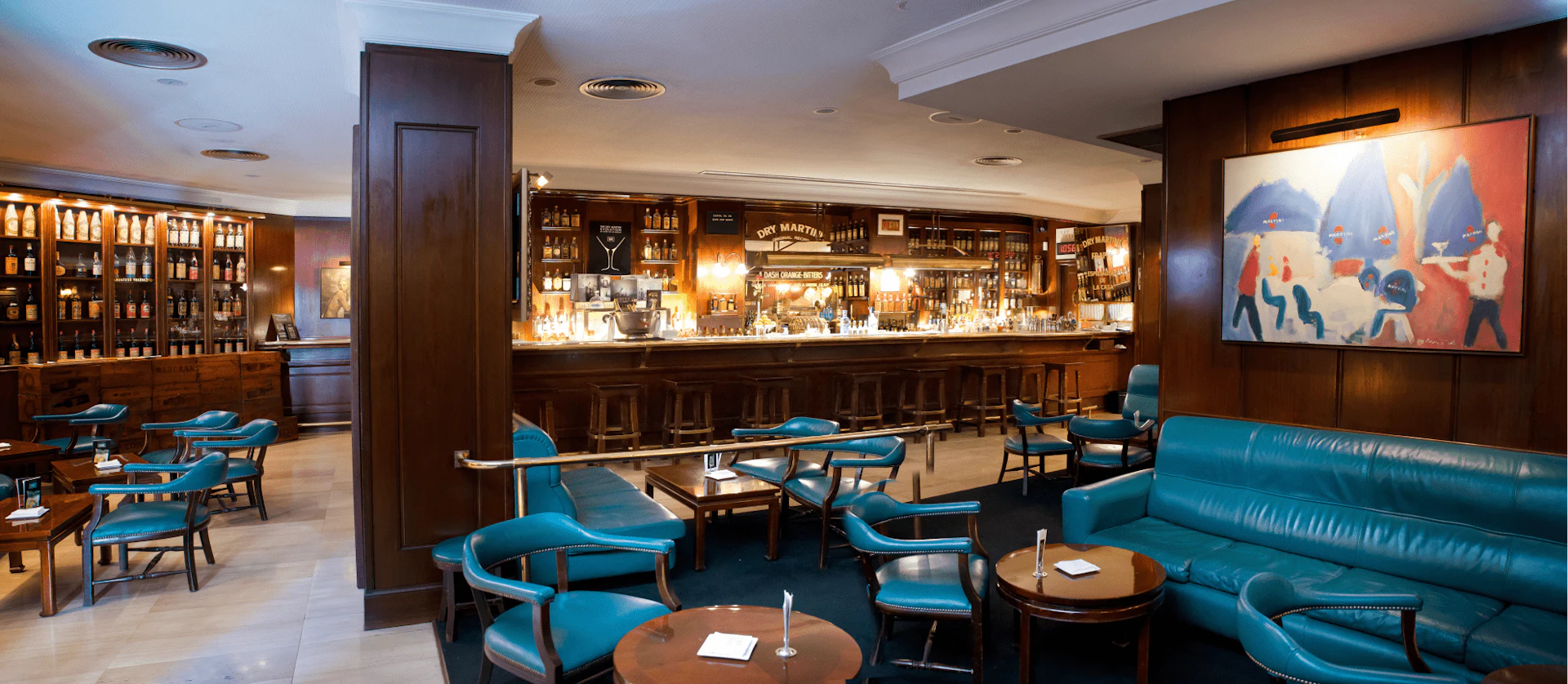 Interior de un bar y salón de lujo con asientos de cuero turquesa, paneles de madera oscura y una barra completamente surtida.