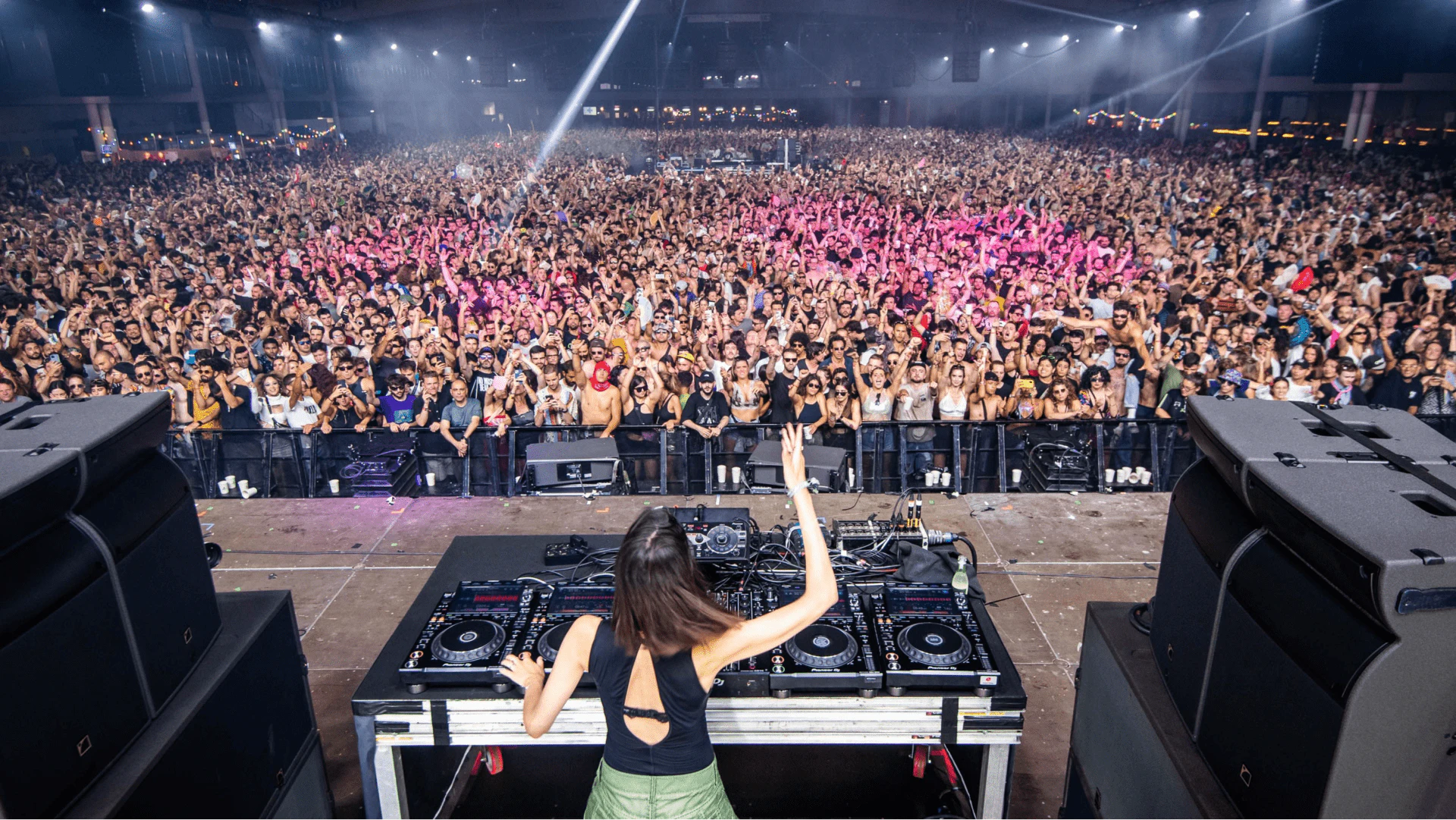 DJ actuando en un gran evento musical en interior con miles de personas bailando y observando entre el público.