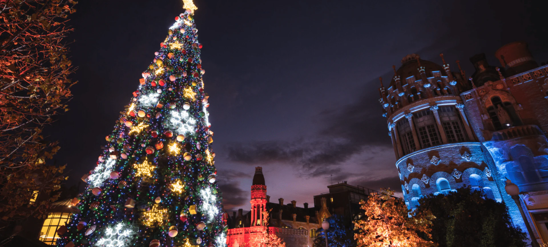 Árbol de Navidad iluminado con adornos de colores en una plaza de la ciudad por la noche.