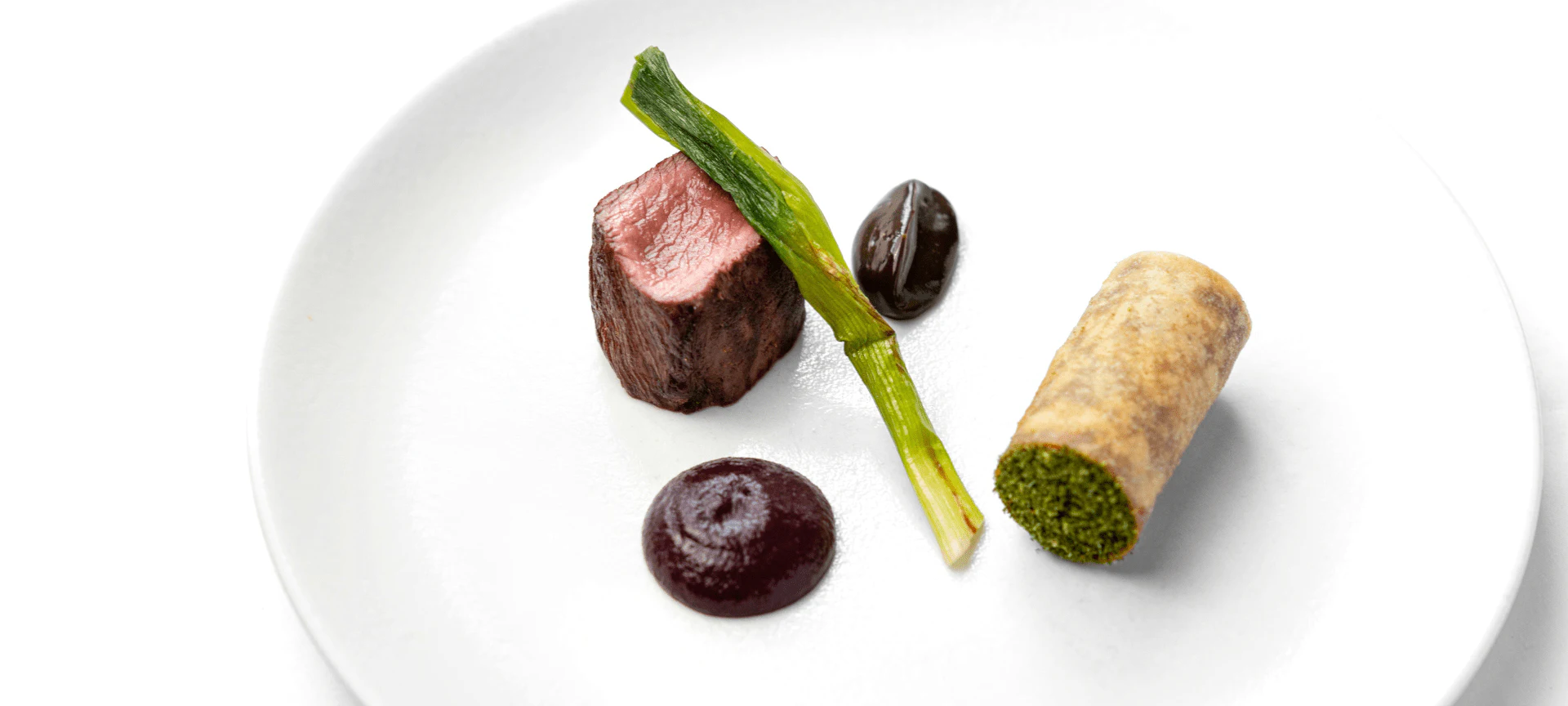 Plato de alta cocina con carne sellada, puré de remolacha, verdura verde, aceituna y rollito de hojaldre relleno de hierbas.
