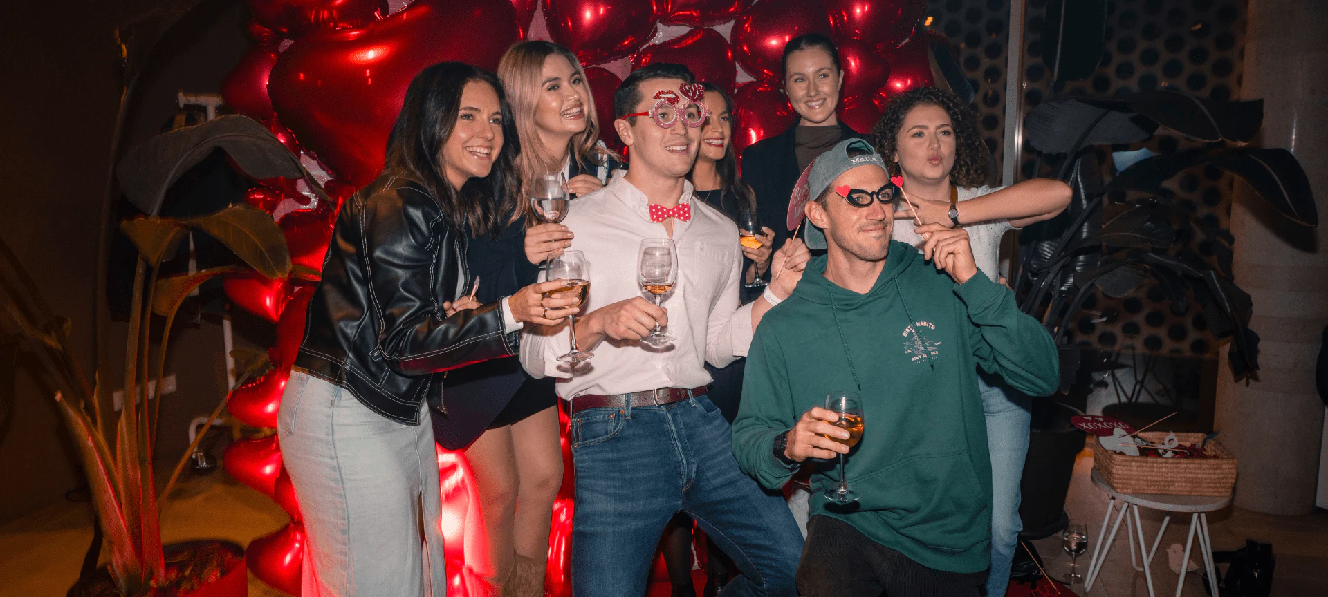 Grupo de personas disfrutando de bebidas y socializando en una fiesta de interior con luces de cordón rojas.