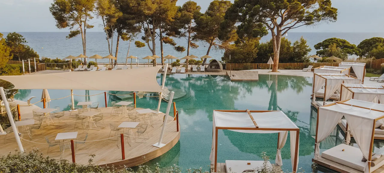 Beach club with a poolside relaxation area, outdoor tables and daybeds overlooking the sea, surrounded by nature on the Costa Dorada near Barcelona.