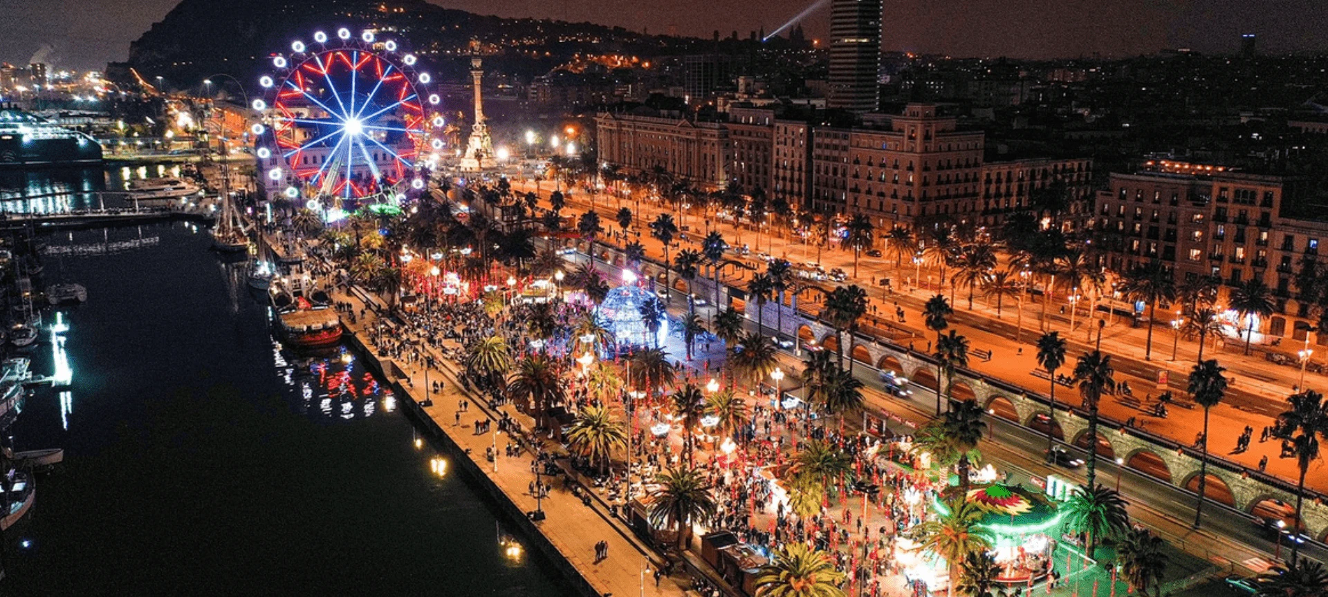 Vista aérea nocturna del paseo marítimo de Barcelona con una noria iluminada y multitudes de personas.