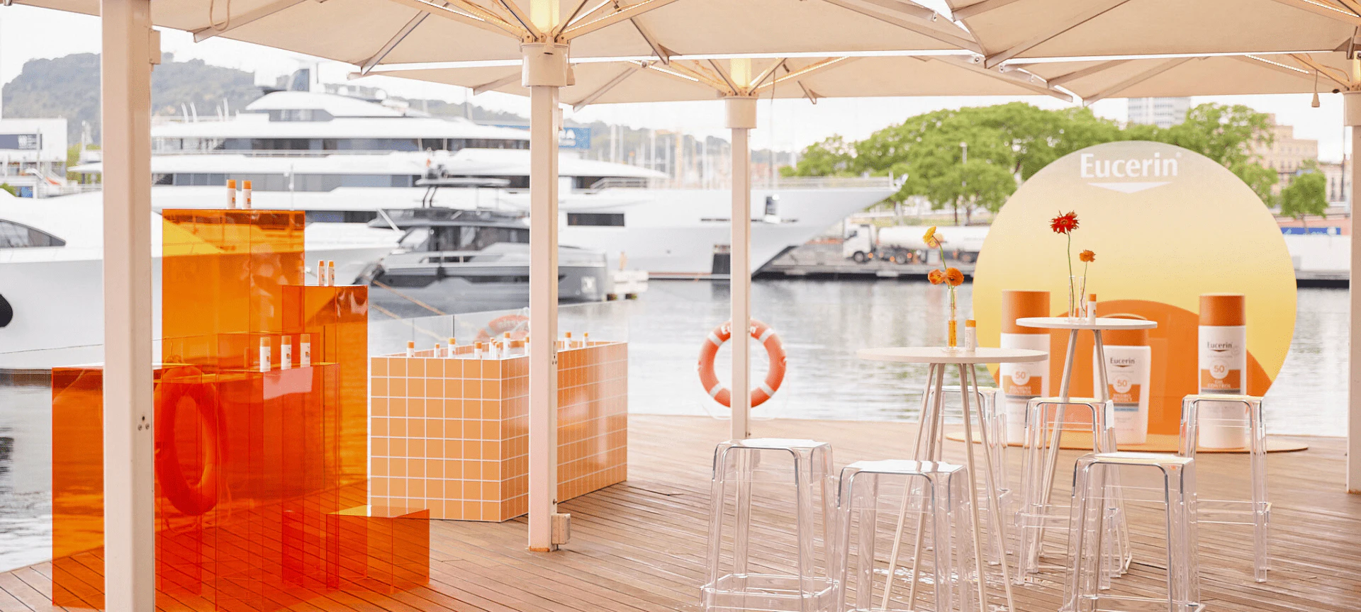 Expositor exterior de marca con elementos de diseño naranja y blanco con vistas a los superyates atracados en un puerto deportivo.