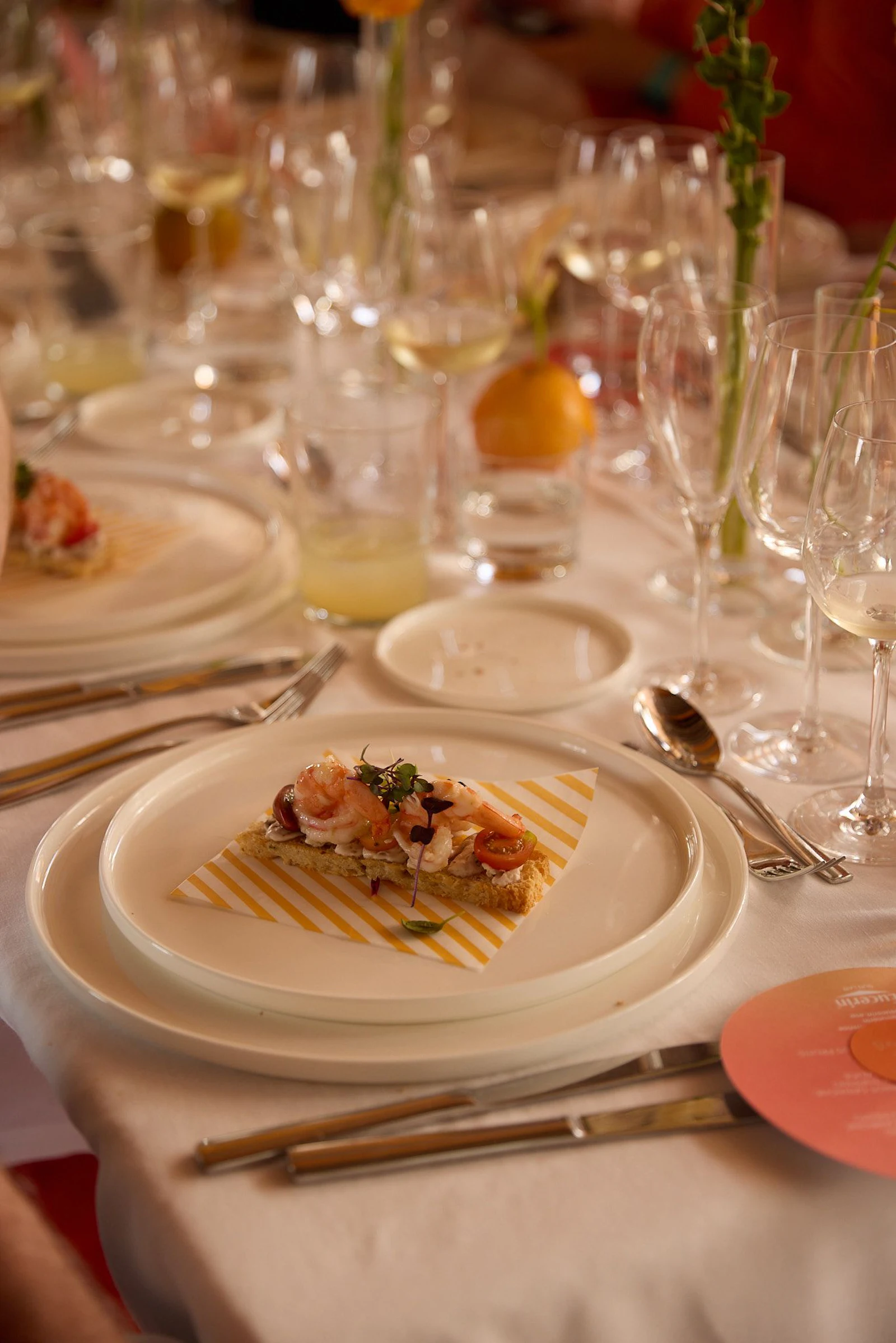 Mesa de comedor formal con un aperitivo de marisco emplatado, copas de vino y cubiertos.