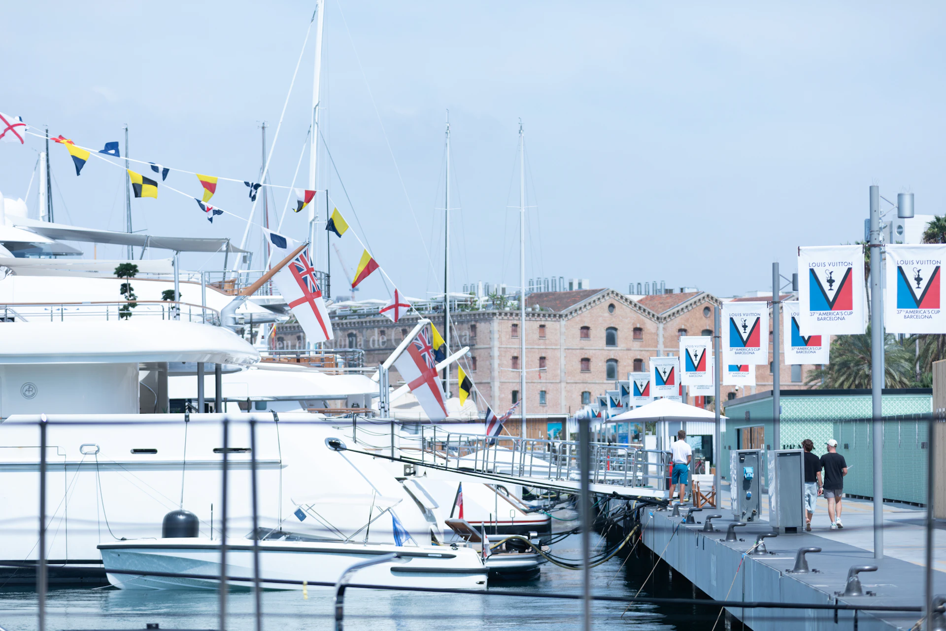 Superyachts and sailboats moored at Marina Port Vell with nautical flags and historic waterfront buildings in Barcelona.