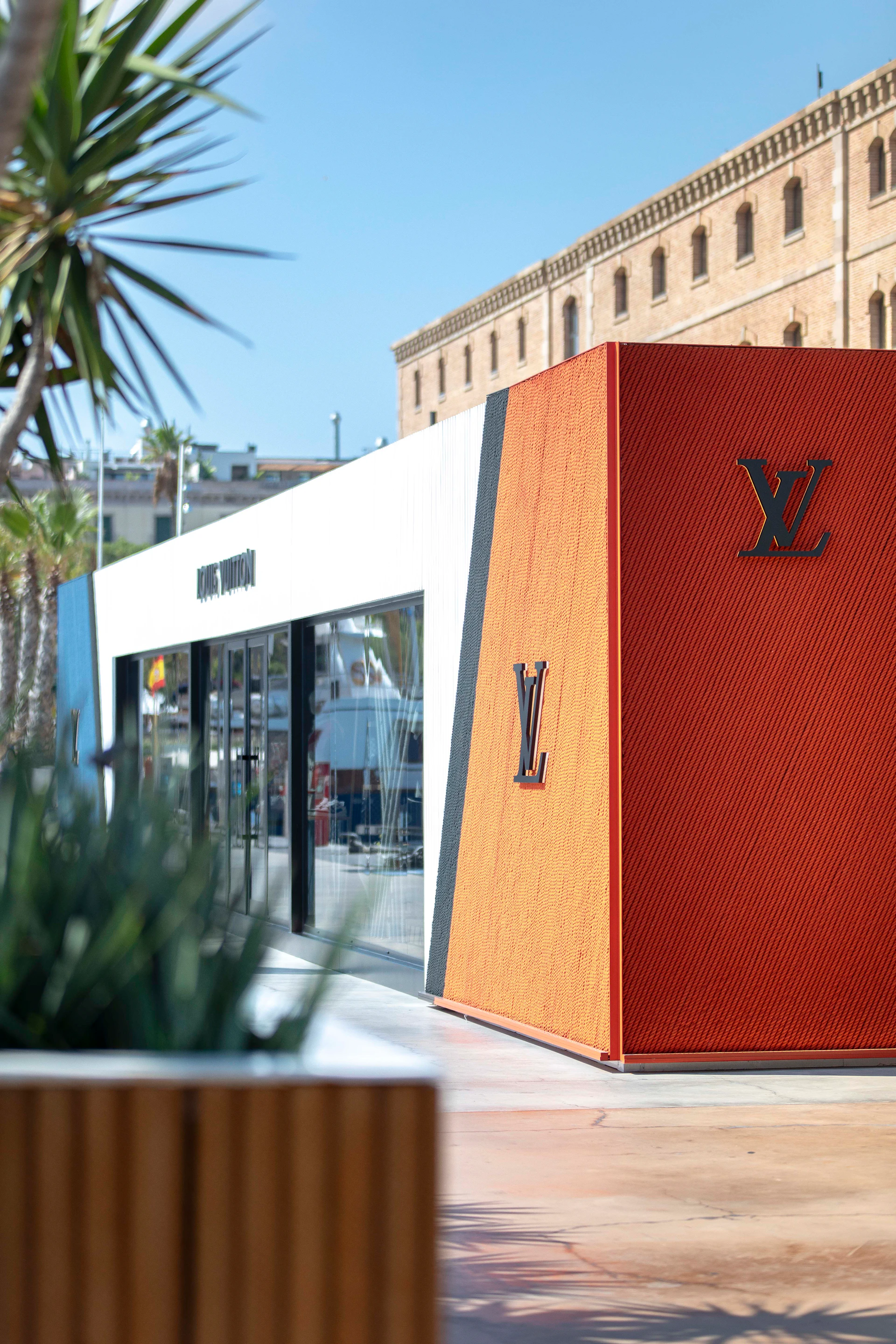 Luxury brand retail store with orange and red corrugated metal facade at a waterfront promenade.