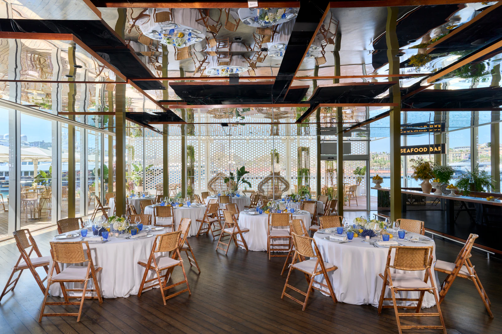 Elegant event space with round tables, wooden chairs, and water views of Barcelona harbor.