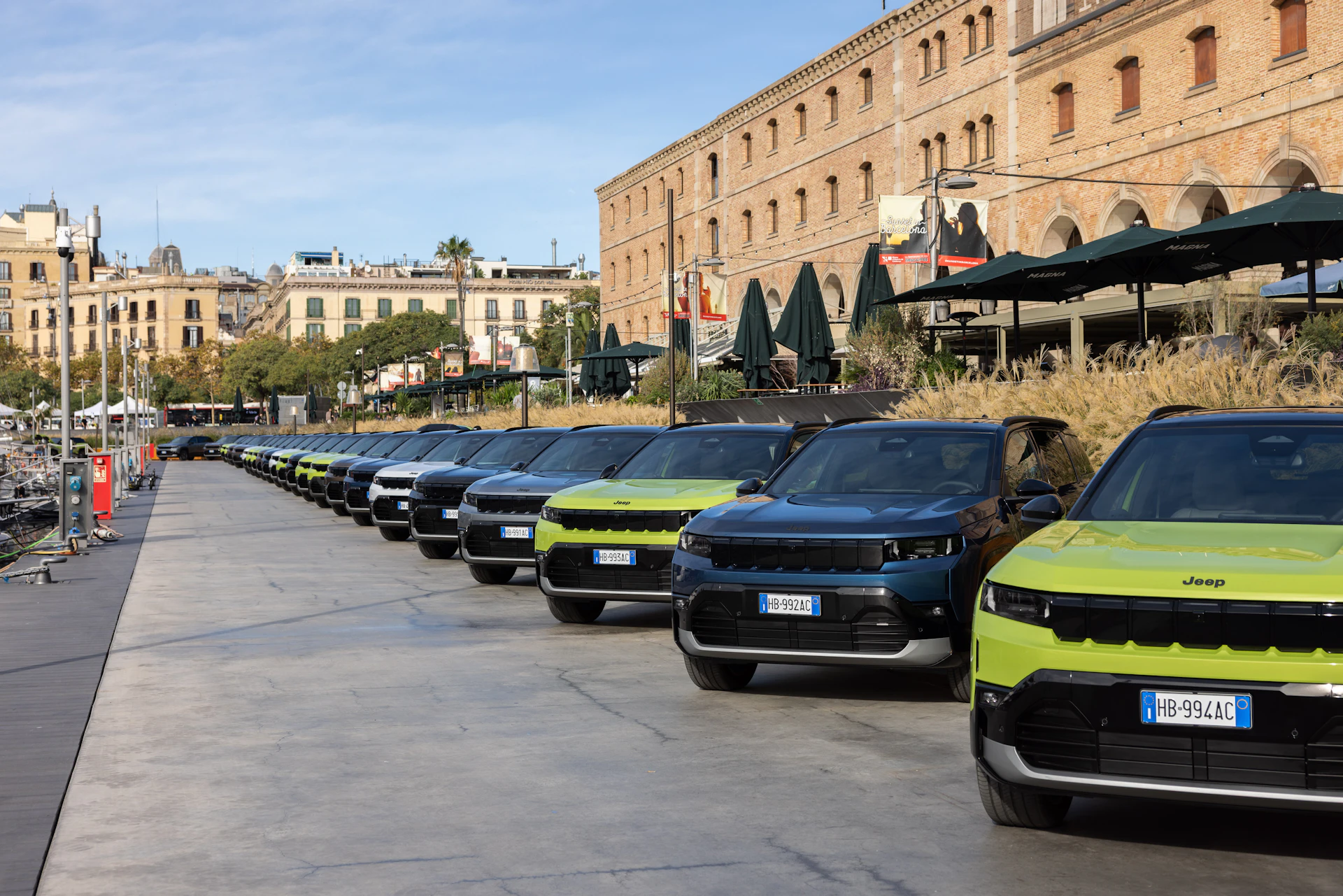 Row of Jeep SUVs parked along a marina promenade with buildings behind.
