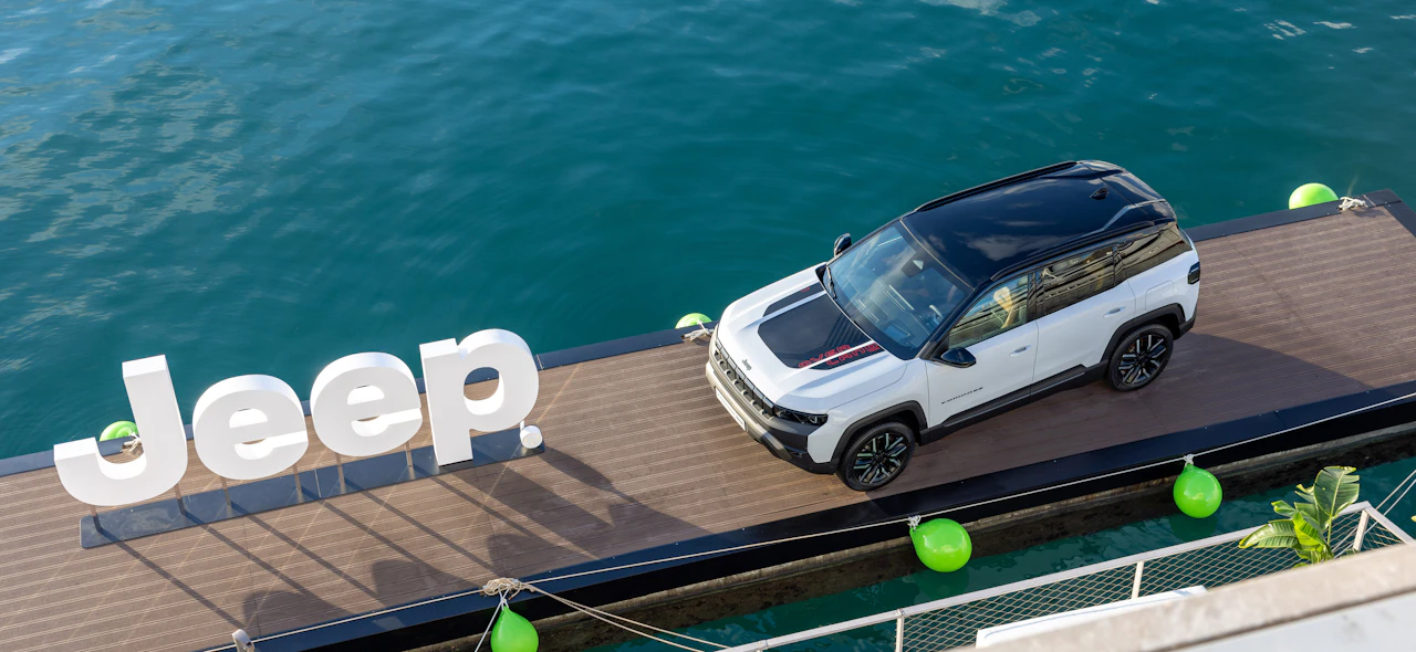 White SUV parked on a marina pontoon beside large Jeep letters over water.