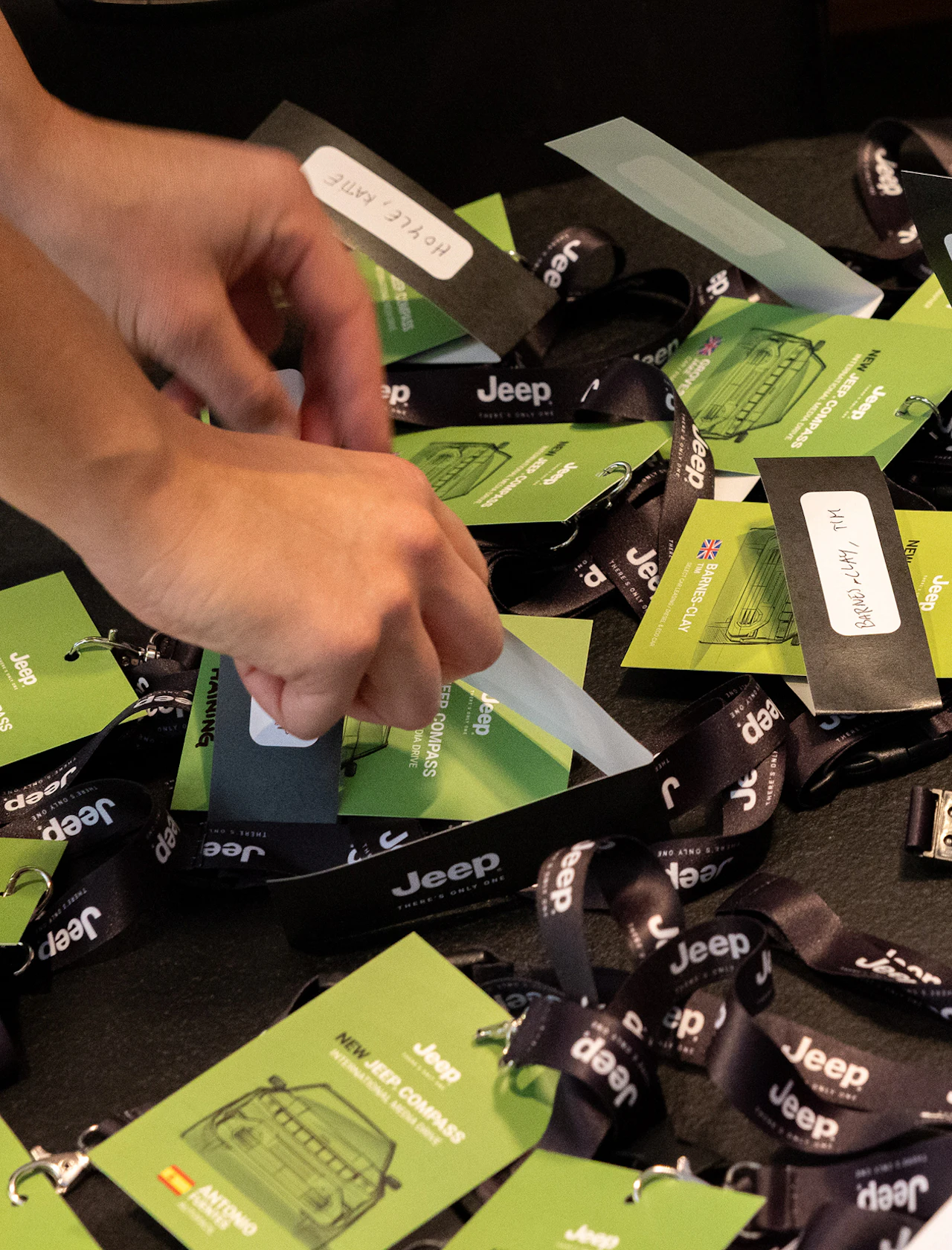 A hand picks up a name badge from Jeep event lanyards laid on a table.