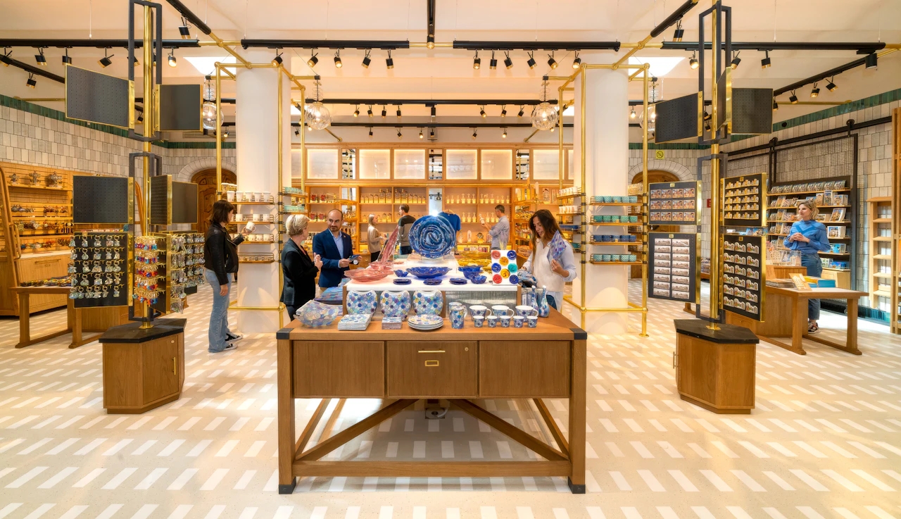 Shoppers browse blue and white ceramics displayed on a wooden table in a shop.