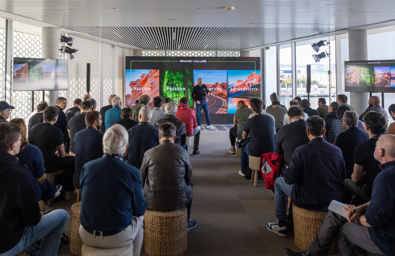 Speaker presents brand values on a screen to a seated audience in a waterfront room.