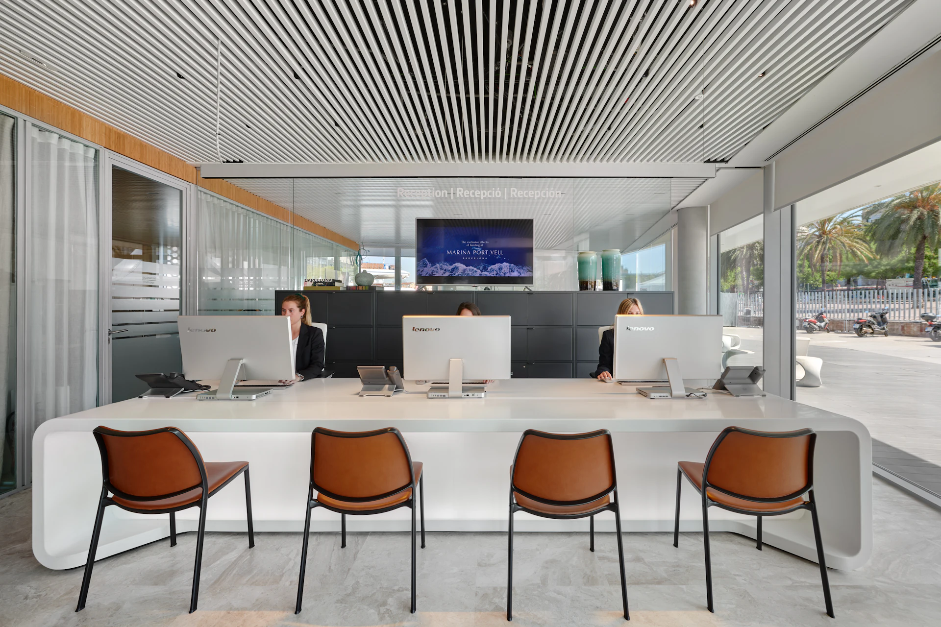 Three staff work at computers behind a white reception desk with leather chairs.