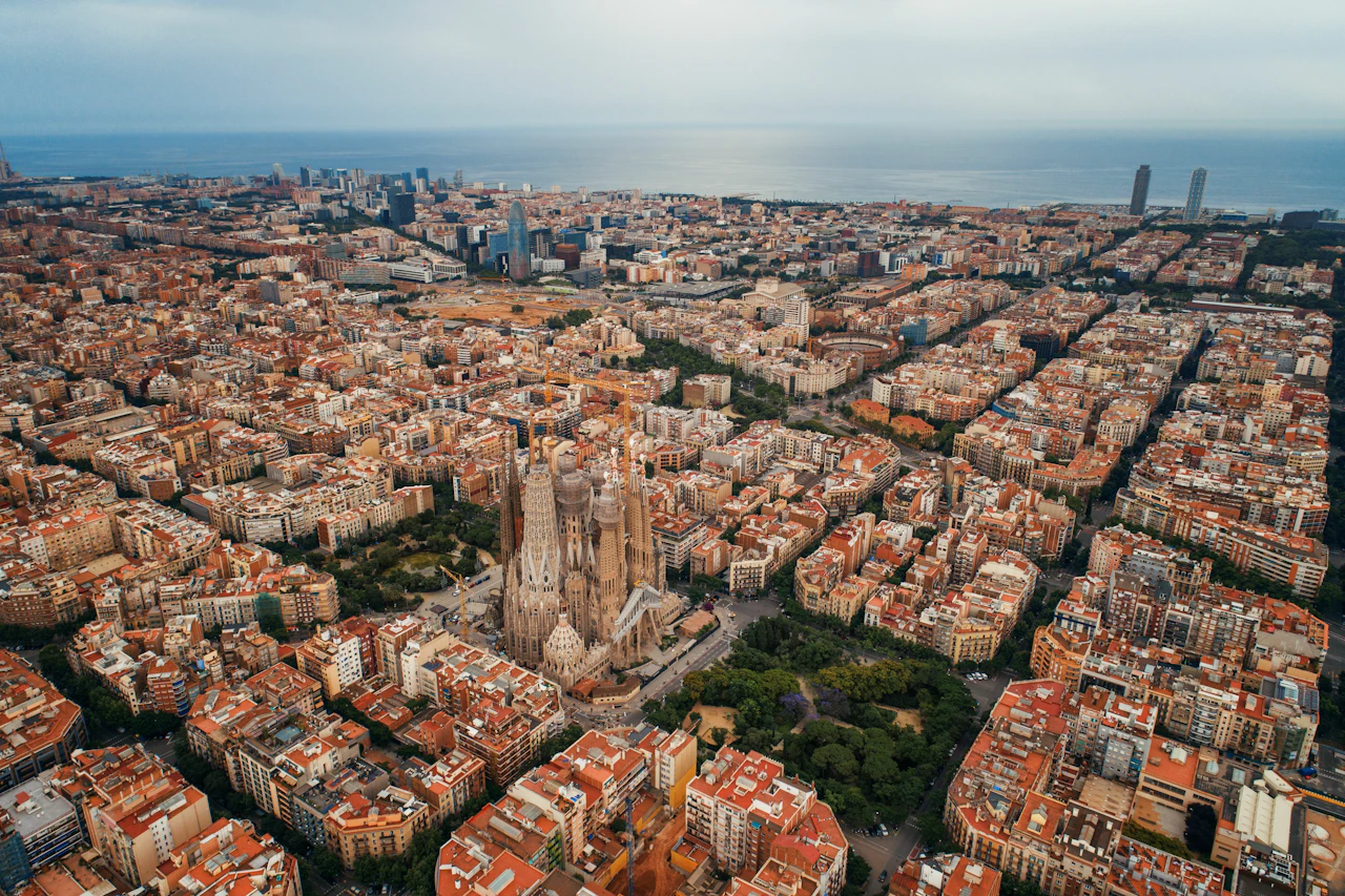 Aerial view of Barcelona cityscape with Sagrada Familia cathedral, Mediterranean Sea, and dense residential buildings.