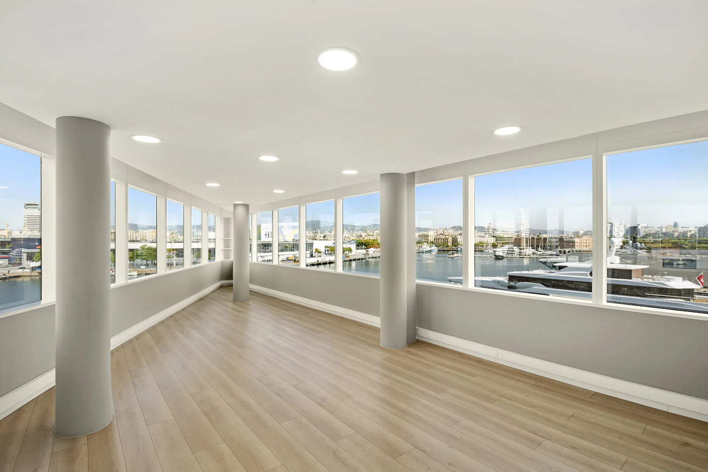 Empty room with wooden floors and large windows overlooking the marina and city.