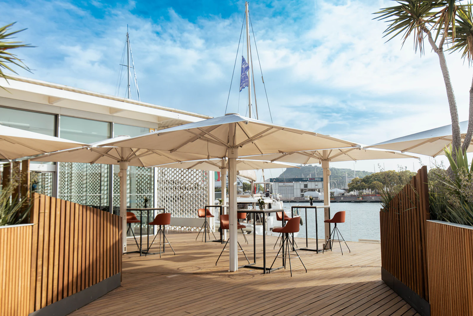 Waterfront terrace with high tables, orange stools and white umbrellas overlooking the marina.