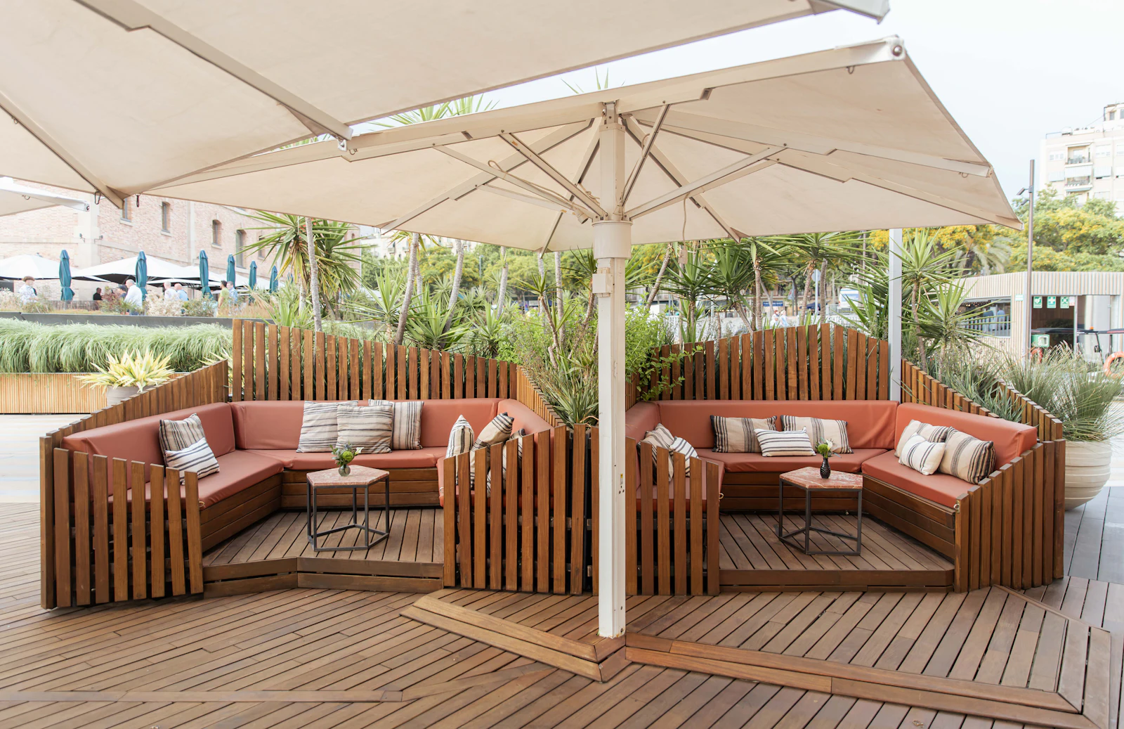 Outdoor lounge area with wooden sofas, cushions, and large umbrellas on a wooden deck.