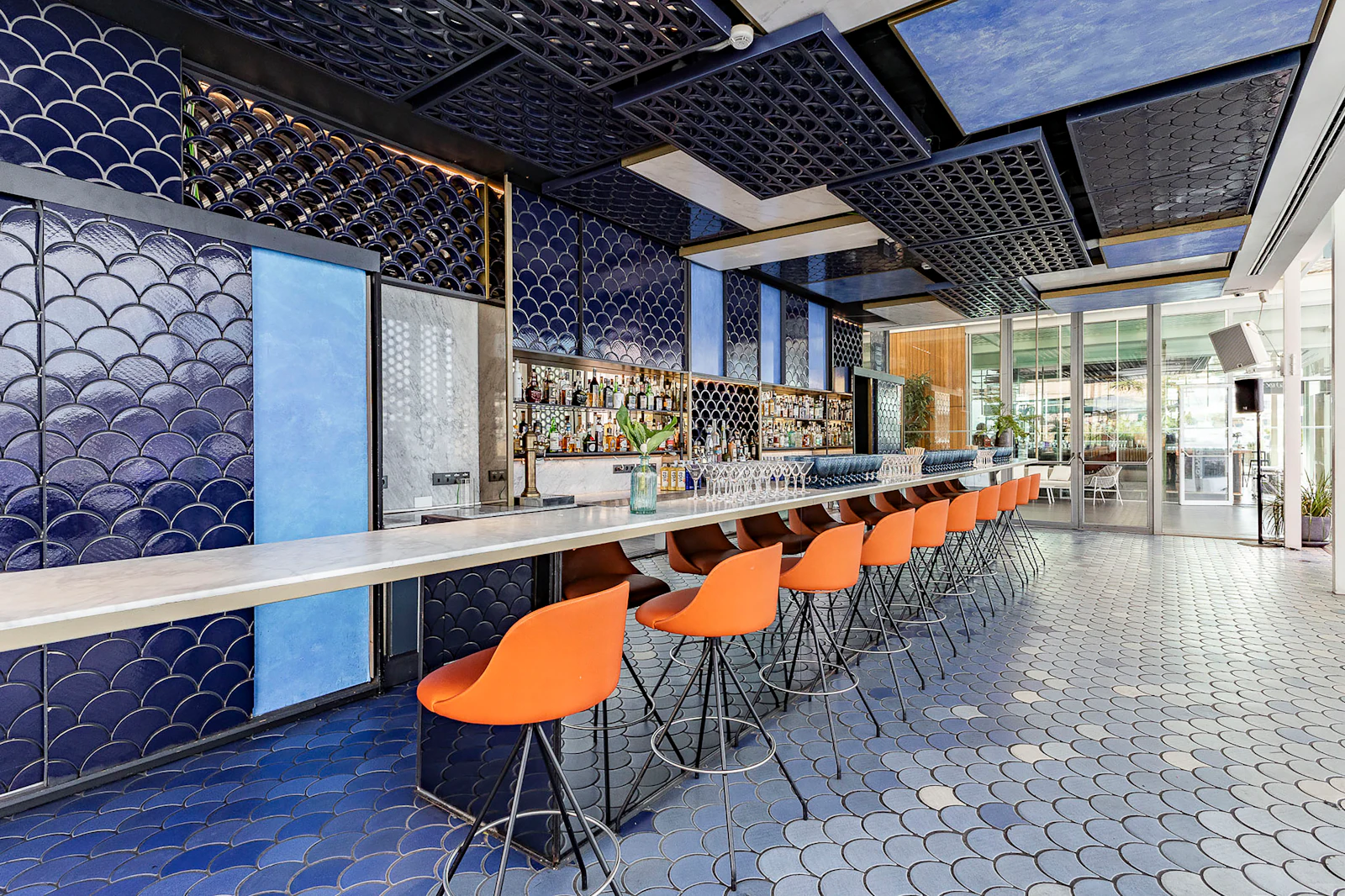 Row of orange stools along a bar with blue fish-scale tiled walls.