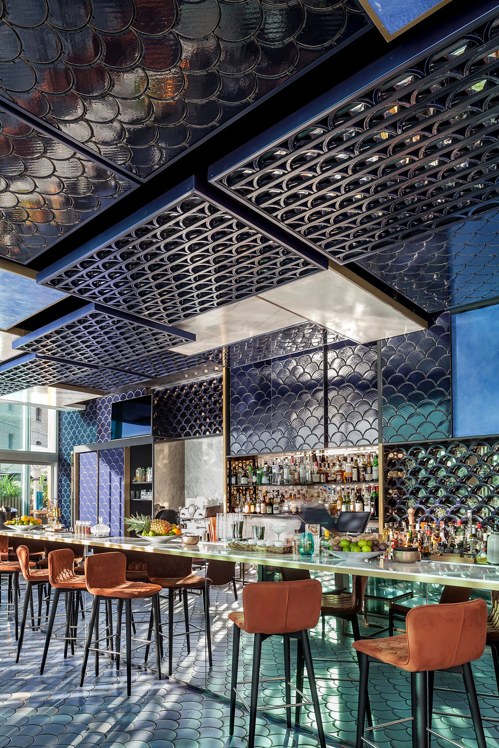 Bar with fish-scale tiled walls and ceiling, leather stools, and shelves of bottles.