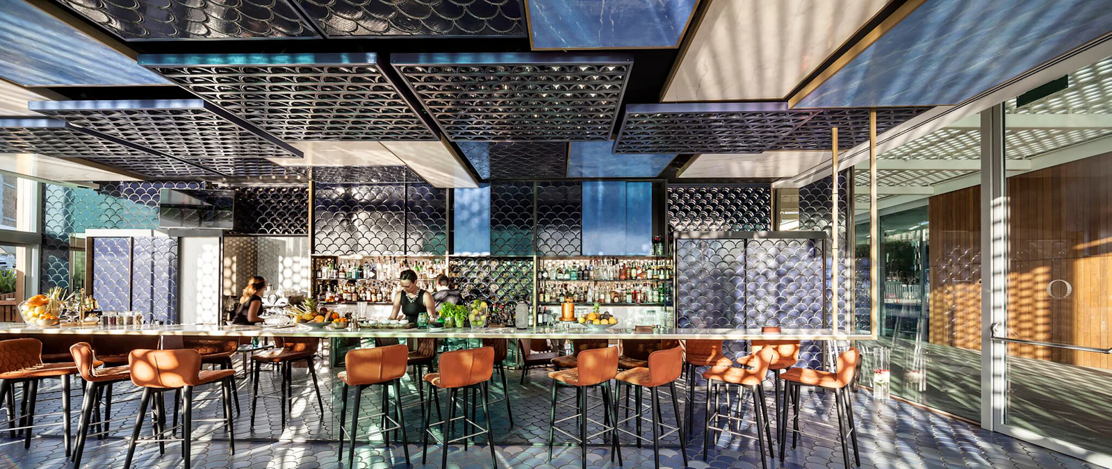 Stylish bar with tan leather stools, patterned tile decor and bartenders serving behind the counter.