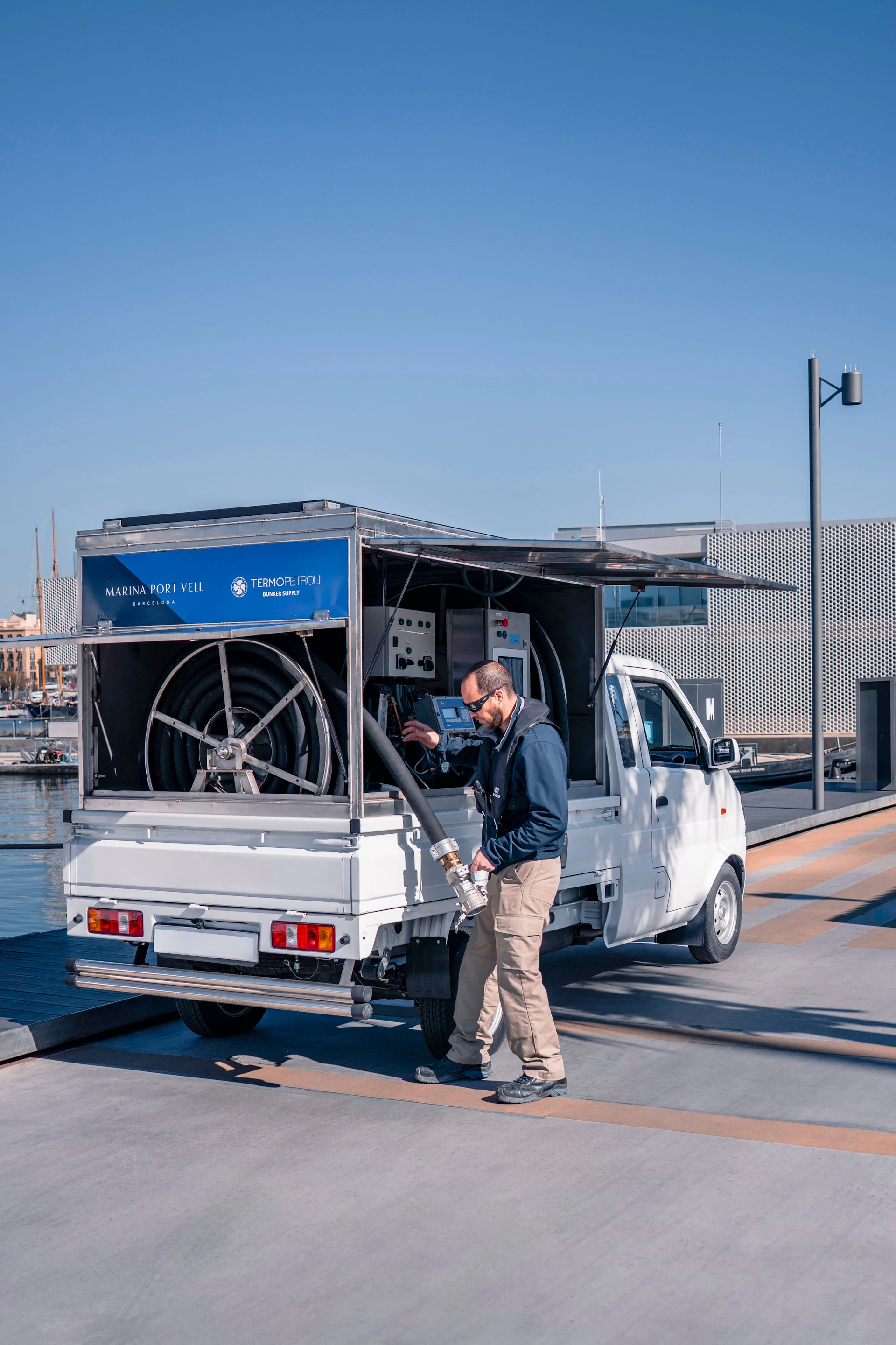 Worker fueling a Marina Port Vell supply truck at the Barcelona waterfront dock.