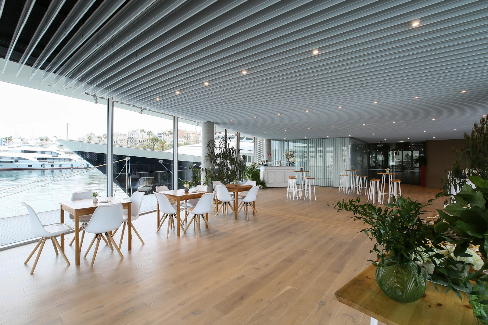 Espacio moderno para eventos con mesas de madera y sillas blancas con vistas a los yates del puerto deportivo.