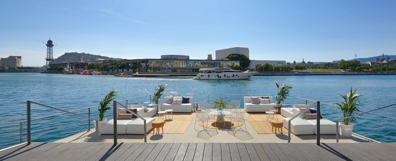 Terraza frente al mar con asientos blancos con vistas a un yate y al puerto de Barcelona.