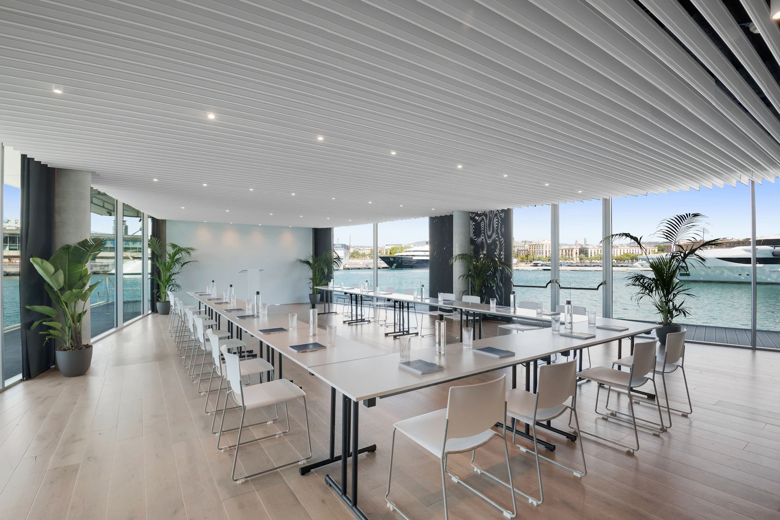 Sala de reuniones con mesa larga y sillas blancas con vistas al puerto deportivo y los yates.