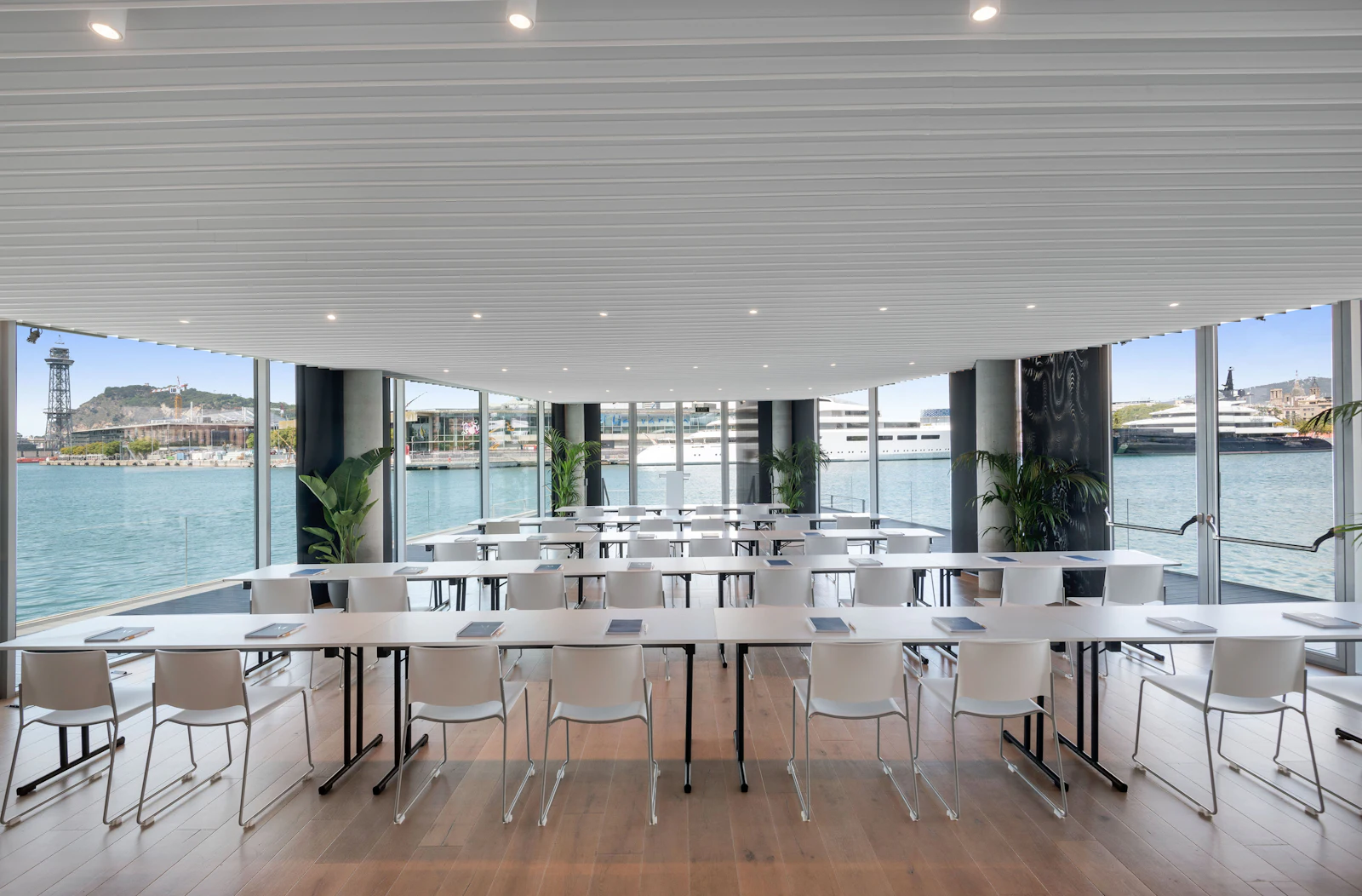 Sala de reuniones con mesas y sillas blancas con vistas al puerto deportivo.