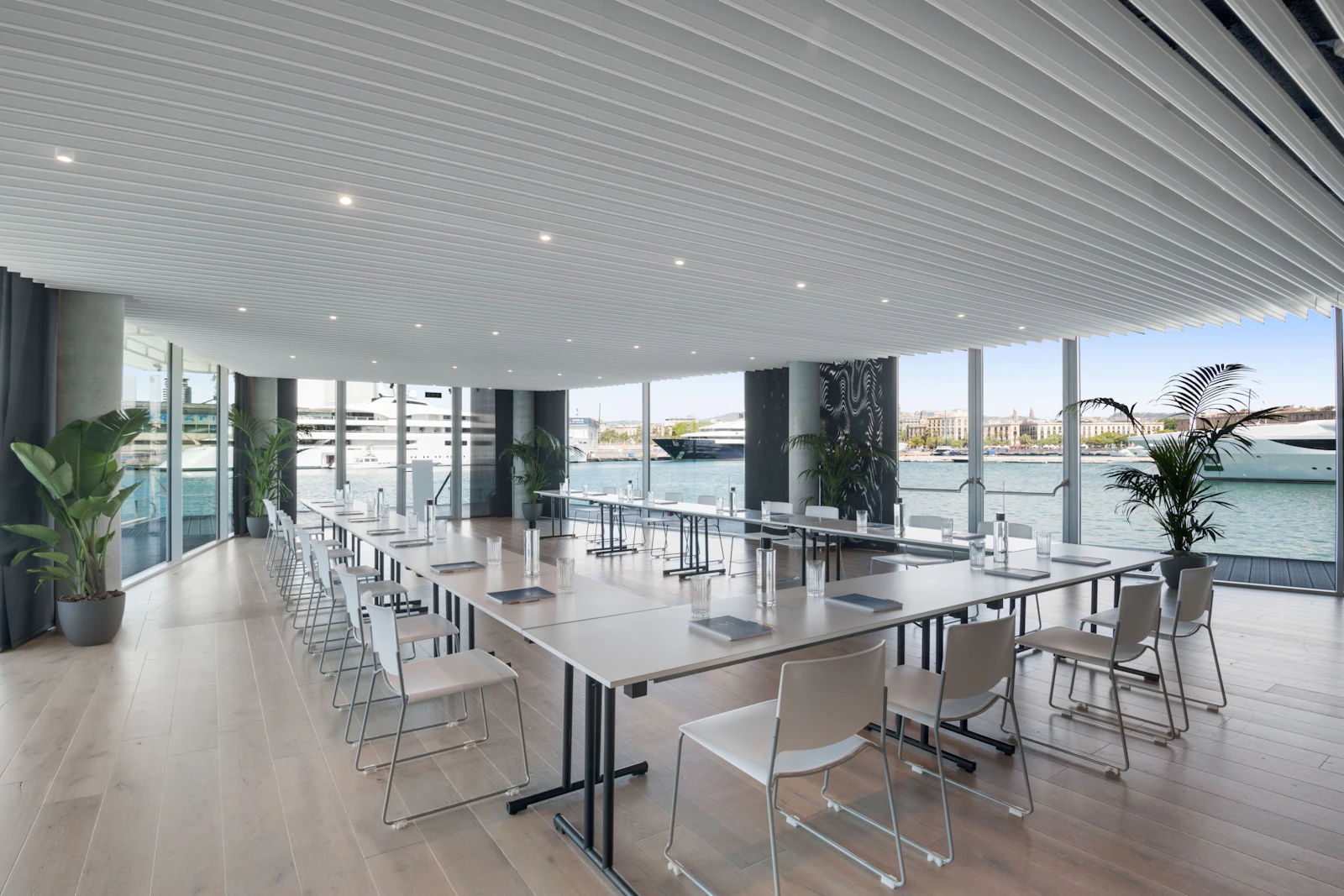 Sala de reuniones moderna frente al mar con mesas largas, sillas y ventanales del suelo al techo con vistas al puerto deportivo de Barcelona.