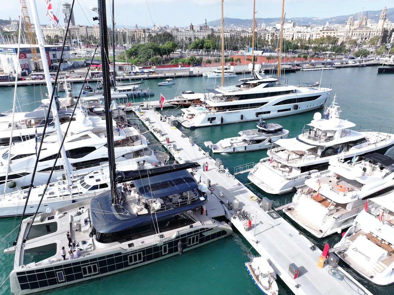 Superyachts and luxury boats moored at Marina Port Vell with Barcelona cityscape and mountains in the background.
